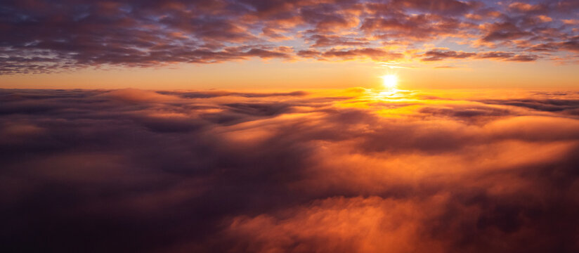 Wide panorama of clouds with setting sun on the background. Aerial drone photo high above the clouds