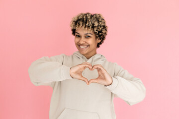 Attractive African American woman making finger heart in studio. Female model with curly hair gesturing. Portrait, studio shot concept