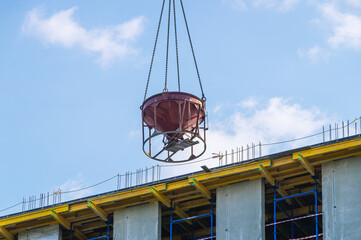 A tower crane lifts a bucket filled with construction cement mortar to a height. The supply of concrete to a height during the construction of buildings and structures. 