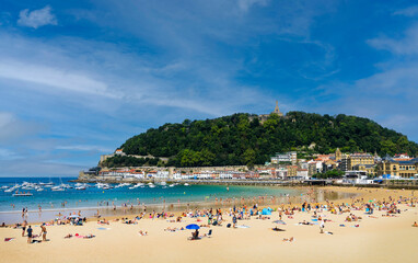 Fototapeta na wymiar Landscape of La Concha beach in the city of San Sebastian, in the Spanish Basque Country, on a sunny day with people enjoying the beach and Mount Urgull in the background.