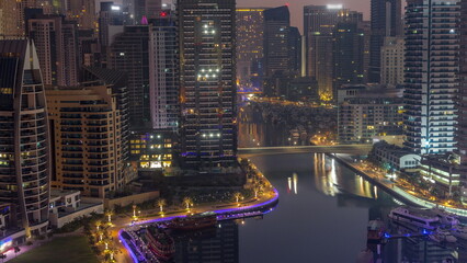 Obraz premium Dubai Marina with several boats and yachts parked in harbor and skyscrapers around canal aerial night to day timelapse.
