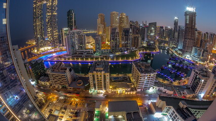 Panorama of Dubai Marina with several boats and yachts parked in harbor and skyscrapers around canal aerial night to day timelapse.