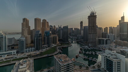 Panorama showing Dubai Marina with several boats and yachts parked in harbor and skyscrapers around canal aerial morning timelapse.