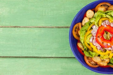 Fresh salad in blue bowl on green wooden table