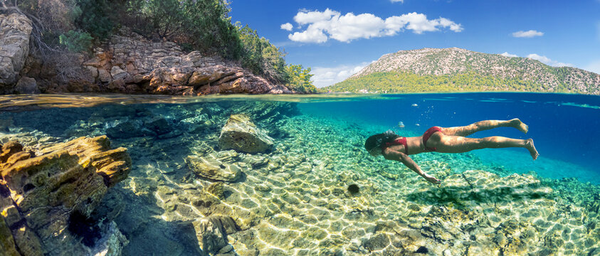 Woman diver is snorkeling on a beautiful sea beach. The lower half of the image is occupied by the seabed, the upper half by the coast and the sky.