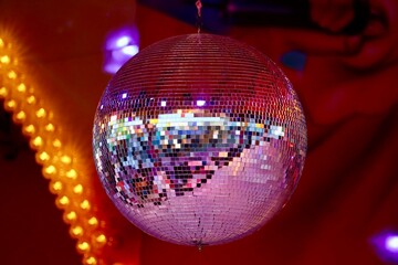 Big disco ball, light reflecting in many cut mirrors, with blurry red and orange lights in background