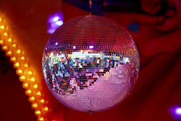 Big disco ball, light reflecting in many cut mirrors, with blurry red and orange lights in...