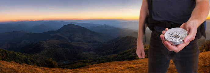 A travel man with backpack holding the compass background on the mountain peak at sunset time