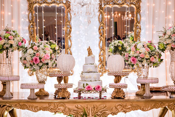 a table decorated with flowers and sweets and a white wedding cake decorated with roses and a golden biscuit wedding couple on top