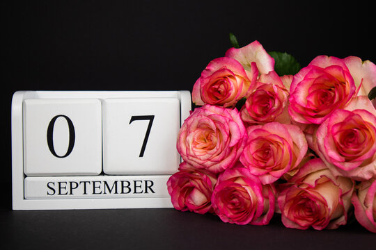 September 7 wooden calendar, white on a black background, pink roses lie nearby.Postcard with copy space. The concept of a holiday, congratulation, invitation, party, announcement, vacation, promotion