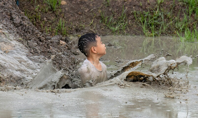 Kid enjoy playing on soil clay slider slide to muddy water below and splash the water in the air...