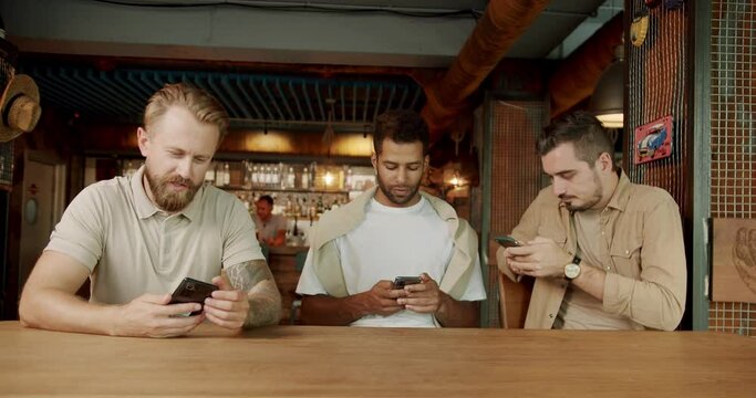 Multiethnic group of people using their smartphones actively. Three friends in a cafe bar using phone. Three men using their smartphones while sitting in pub after work.