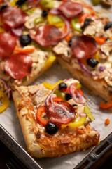 A piece of square pizza with basil pepperoni tomatoes and mushrooms on a iron tray
