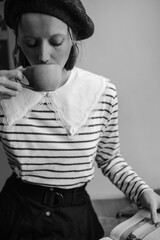 Stylishly dressed young woman in a beret drinking coffee and reading a book. Parisian coffeeshop vibe