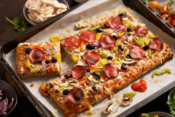 A piece of square pizza with basil pepperoni tomatoes and mushrooms on a iron tray