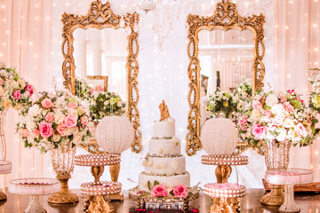 a table decorated with flowers and sweets and a white wedding cake decorated with roses and a golden biscuit wedding couple on top