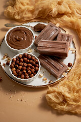 Chocolate popsicles with hazelnuts served with melted chocolate on a white plate