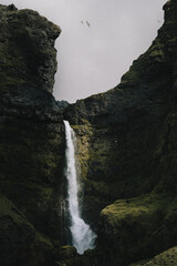 Fototapeta na wymiar Small waterfall with beam of sunlight set back amongst rocky cliffs
