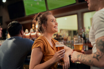 Woman drinking beer in bar and talking with man