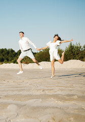 Cheerful couple running on the sand holding hands.