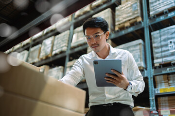 Portrait of Asian Chief Engineer checking product details and supplies on shelf with stock in warehouse background. Logistics warehousing and export concept of logistics business