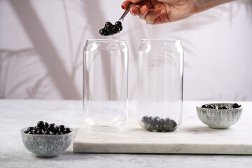 Female hand putting cooked tapioca pearls for trendy bubble boba ice tea into a transparent empty...