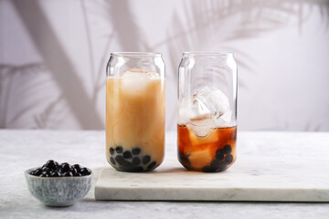 Two glasses with black tea, milk, ice cubes and cooked tapioca pearls for trendy bubble boba ice...