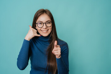 Call me! Attractive cheerful Italian woman in glasses and blue sweater smiling, pointing at camera,...