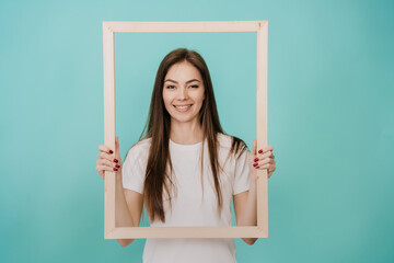 Young Italian woman with long hair in a white T-shirt stands on a turquoise background, holds a...