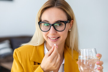 Happy woman holding vitamin capsule and glass of water looking at camera and smiling friendly,...