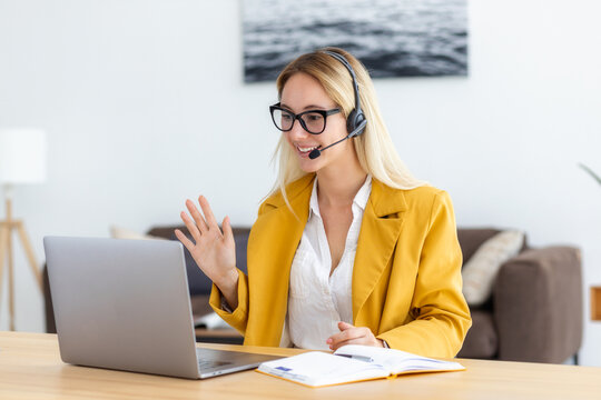 Young woman in headset having in video meeting communicates with employees or the client online using laptop computer. Smiling female agent or support worker consults a client