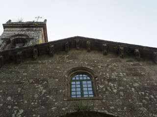 colecci&oacute;n de antiguos canecillos adornando la cornisa de la iglesia de santa susana de santiago de compostela, debajo ventana acristalada con arco de medio, detr&aacute;s el campanario rom&aacute;nico, la coru&ntilde;a