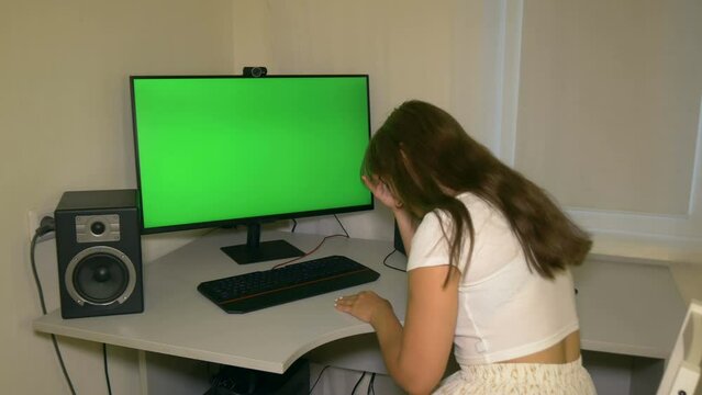 Girl is very sad with what is shown on the computer screen. Chromakey on computer screen. Video with a chroma key on the screen to insert any video or image.