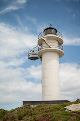 A white lighthouse on top of a hill with a blue sky with clouds