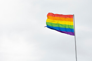 Rainbow flag, a symbol for the LGBT community, waving in the wind with a cloudy white background