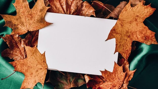 4k zoom in out Mock up Greetings typing background Green color silk cloth with autumn leaves, white paper and fall leaves Flat lay composition for greeting cards Season image Copy space