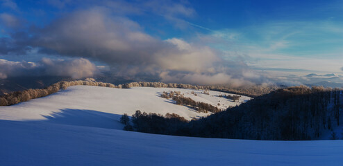 Couds over a winter mountain valley. Panorama of a mountain plateau covered with snow.