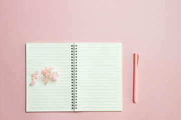 A white notebook with flowers and pink pen on pink background. 