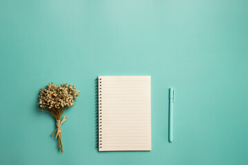 A white book with flowers and pen over the mint background. 