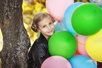 Fototapeta na wymiar Cute smiling little girl with colorful balloons in autumn park, birthday celebration
