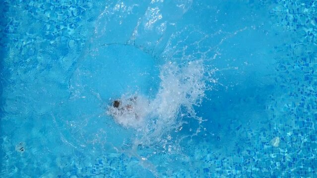 Top view of young woman jumping in pool and splashing crystal clear water. Unrecognizable girl resting and having fun on resort. Lady relaxing during summer vacation or holiday. Slow motion Close up