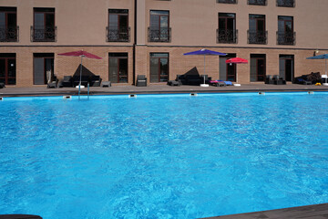 Blue large swimming pool at the modern hotel building in the resort in summer with umbrellas from the sun
