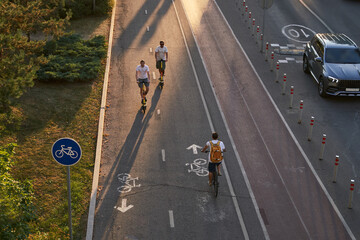 Top aerial view of cyclist and two mans are riding on kick scooters on cycling road.