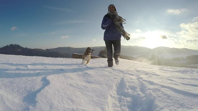 4K woman running with her beagle outside on snowy hill jumping and shouting. Animals, environment, spending time outside, winter sports concept.