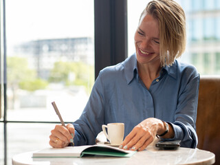 Elegant smiling woman in a coffee shop writing in a notebook. Organization ,business woman