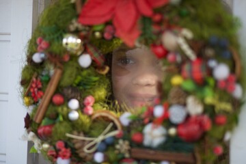 girl peeking behind a Christmas wreath. High quality photo