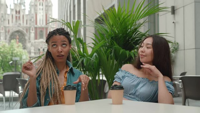 Afro woman showing asian female a ring of getting marriage. Friend is jealous of the news. Two friends sitting in cafe in outdoor