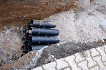 lot of new black pipes for protecting electrical wires in trench on street, concept of repairing...