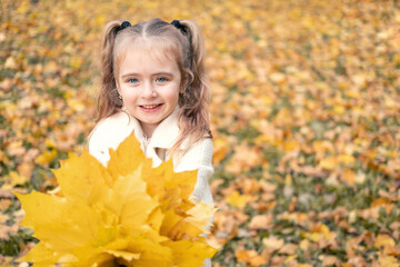 smiling happy little child girl in coat and dress holding autumn leaves, having fun in fall forest