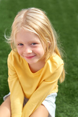 Pretty blonde girl yellow t shirt sitting on green grass. Top view.